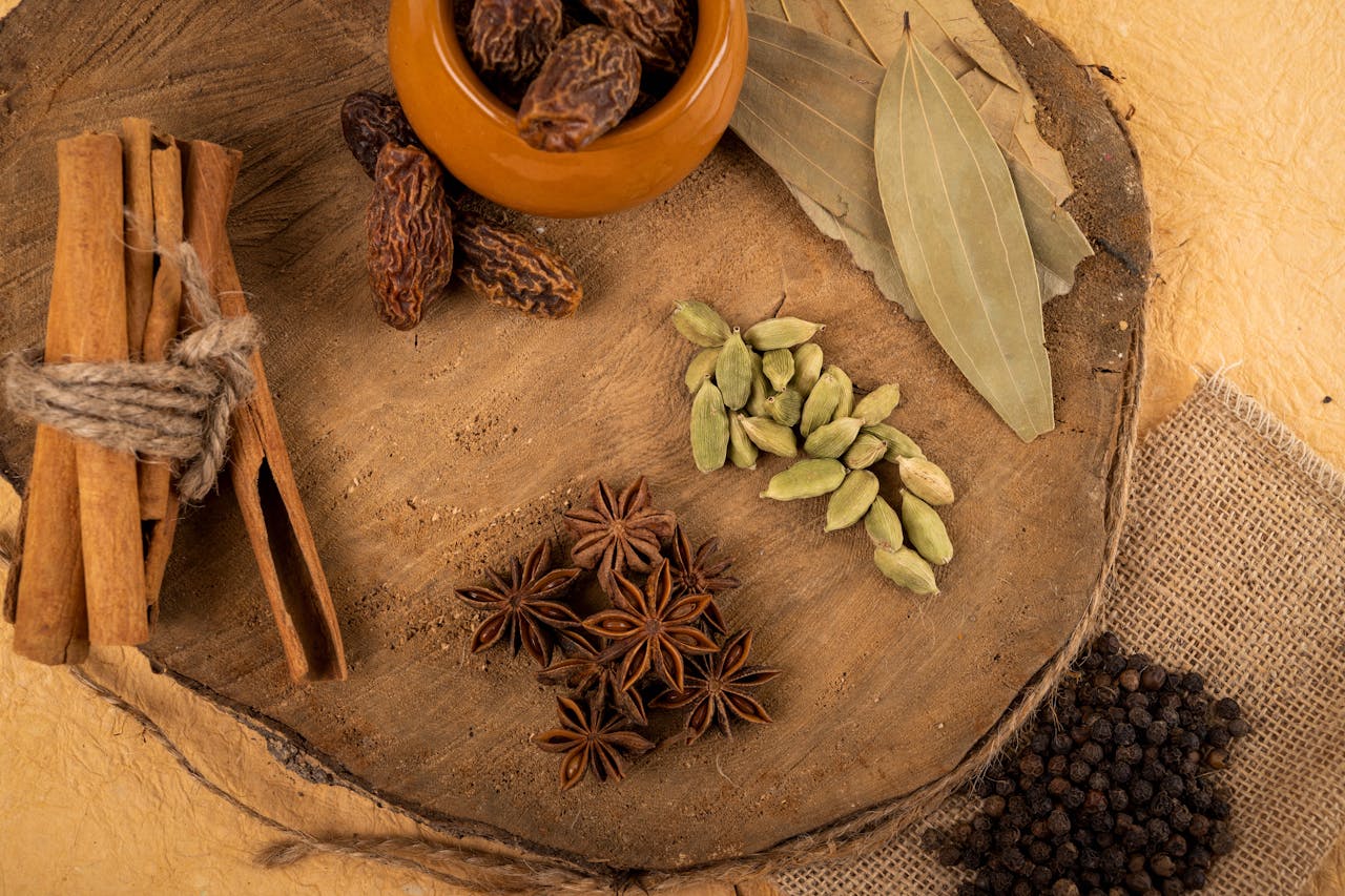 A collection of Indian spices including cardamom, star anise, and bay leaves on a wooden board.