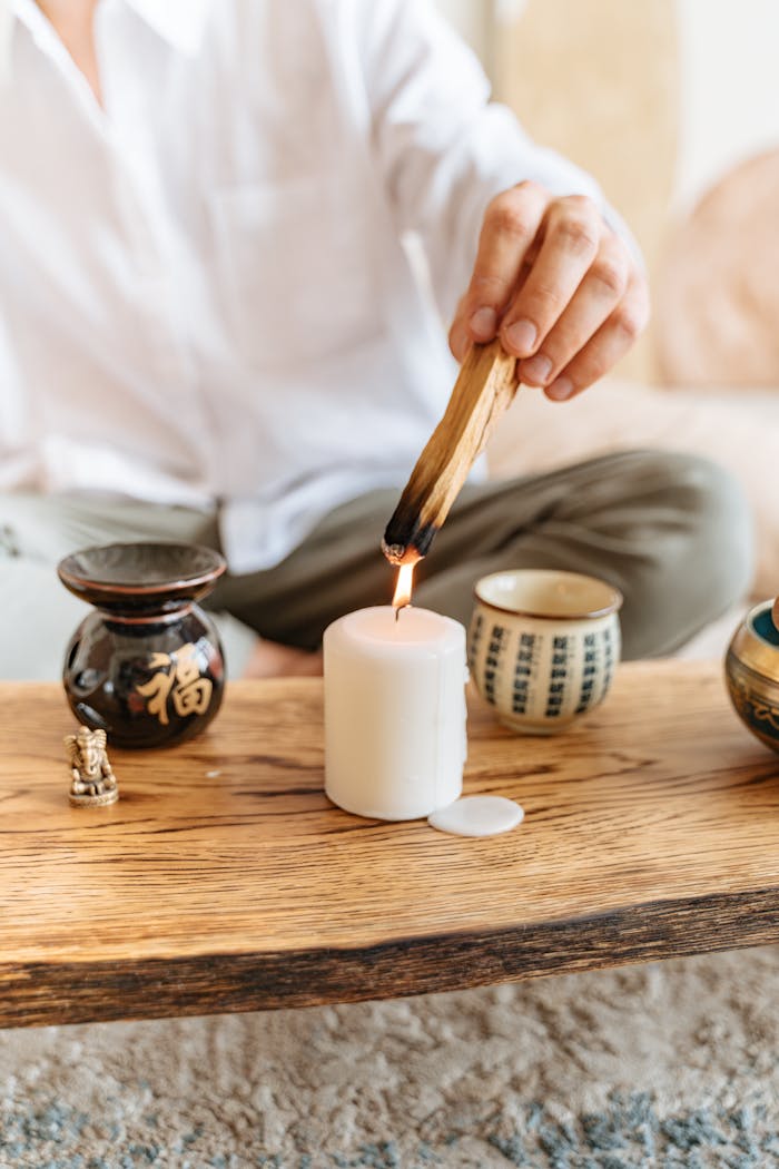 A serene setup of a person using palo santo for aromatherapy with a candle on a wooden surface.