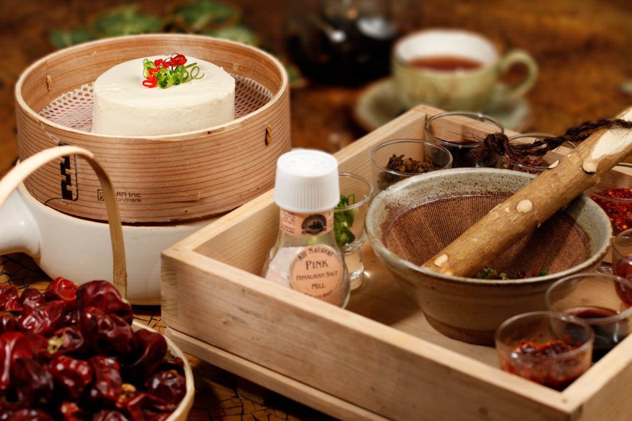 A close-up of culinary ingredients with a mortar and pestle on a wooden tray, featuring tofu and spices.